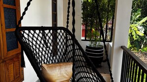 A hanging chair with a cushioned seat and a netted back, positioned on a balcony with a railing and a potted plant nearby. - Tranquil 2-bedroom house with AC in delightful Varkala (Varkala)
