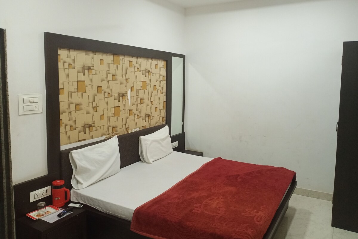 Habitación de hotel con cama, mesita de noche, manta roja, pared con estampado geométrico y ventilador de techo.
