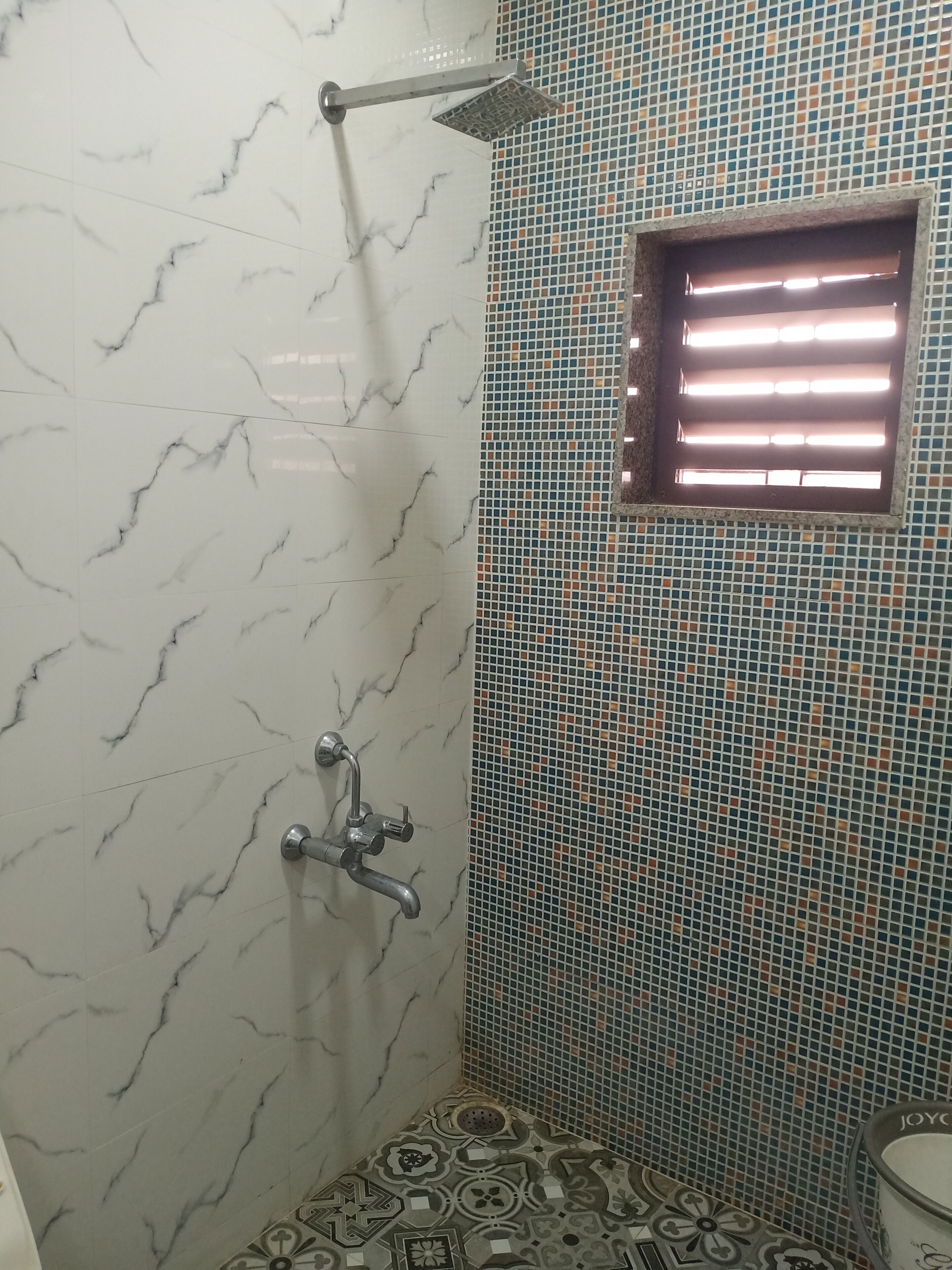 A bathroom with a shower, a window, and patterned tiles.