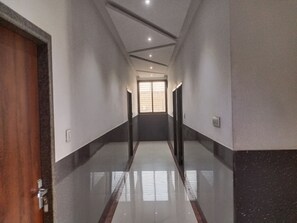 Un pasillo con una puerta de madera a la izquierda, una ventana al final y otra puerta a la derecha.