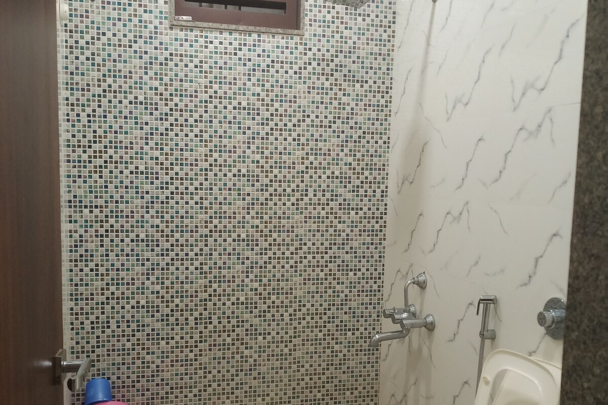 Baño con inodoro, ducha y un taburete rosa pequeño.
