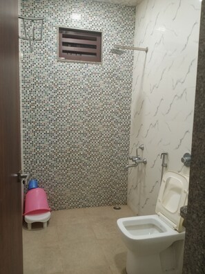 Baño con inodoro, ducha y un taburete rosa pequeño.
