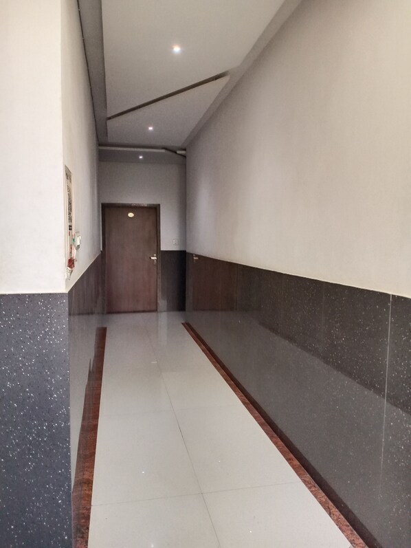 A corridor with a tiled floor, a wooden door at the end, and a wall with a dark and light panel design.