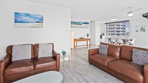 A living room with two brown leather sofas, a glass coffee table, and a dining area with a wooden table and chairs. - Iconic Burleigh Beachfront, 2 Bedroom Apartment (Gold Coast)