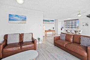 A living room with two brown leather sofas, a glass coffee table, and a dining area with a wooden table and chairs. - Iconic Burleigh Beachfront, 2 Bedroom Apartment (Gold Coast)