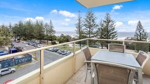 A balcony with a table and chairs, overlooking a parking area and a view of the ocean. - Iconic Burleigh Beachfront, 2 Bedroom Apartment (Gold Coast)