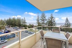 A balcony with a table and chairs, overlooking a parking area and a view of the ocean. - Iconic Burleigh Beachfront, 2 Bedroom Apartment (Gold Coast)