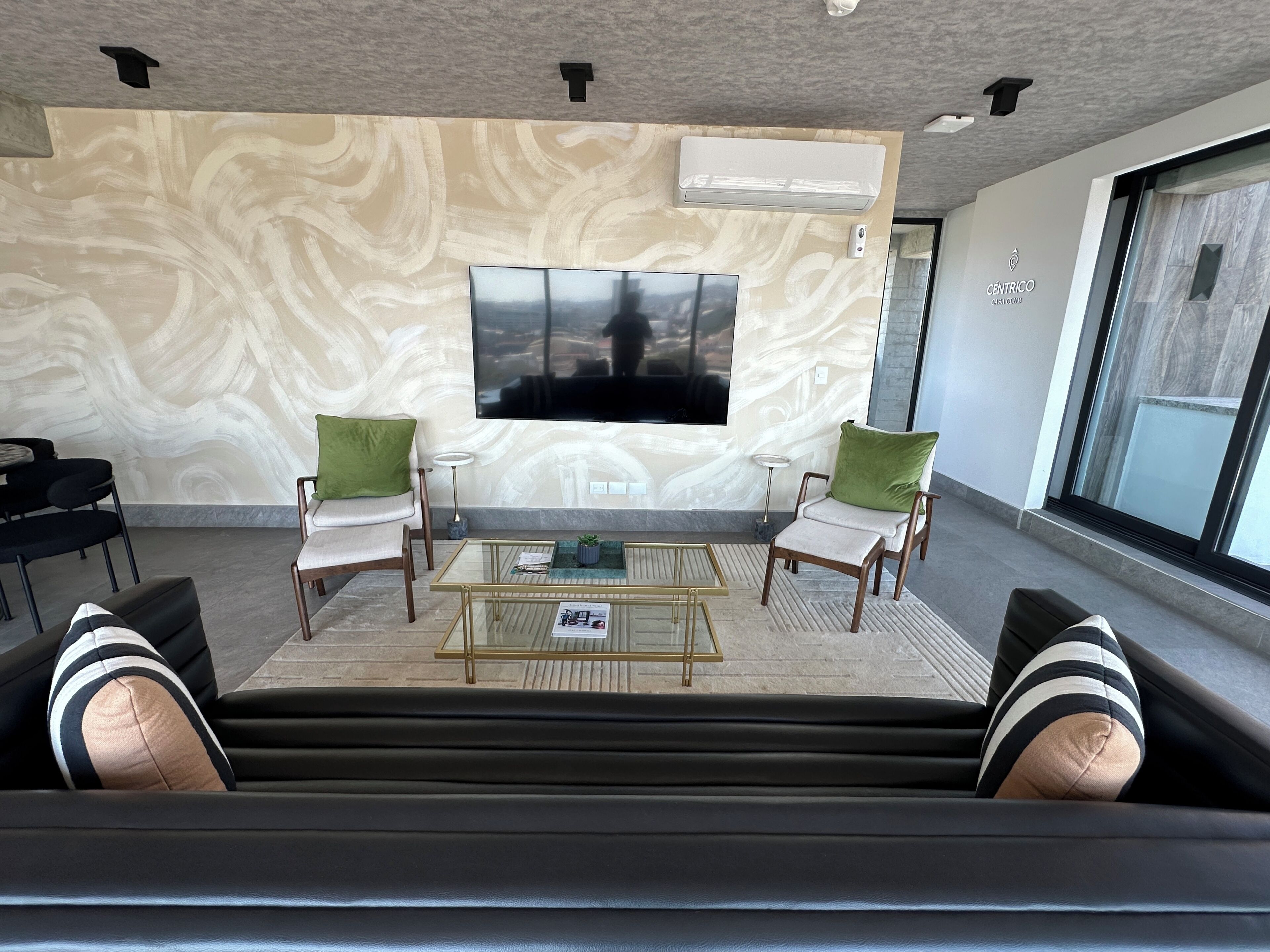 Uma sala de estar moderna com uma televisão de tela plana grande, duas poltronas, uma mesa de centro e uma parede com padrão.