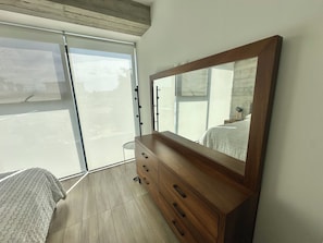 A bedroom with a large mirror, a wooden dresser, a bed, and a sliding glass door. - Sleek Modern Condo in Downtown Tijuana - Free Parking, 24/7 Security, and Rooftop (Tijuana)