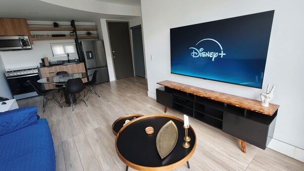A modern living room with a flat-screen TV, a dining area, and a kitchenette. - Sleek Modern Condo in Downtown Tijuana - Free Parking, 24/7 Security, and Rooftop (Tijuana)