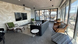 A modern living room with a large flat-screen TV, comfortable seating, and a view of the city through large windows. - Sleek Modern Condo in Downtown Tijuana - Free Parking, 24/7 Security, and Rooftop (Tijuana)