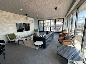 A modern living room with a large flat-screen TV, comfortable seating, and a view of the city through large windows. - Sleek Modern Condo in Downtown Tijuana - Free Parking, 24/7 Security, and Rooftop (Tijuana)