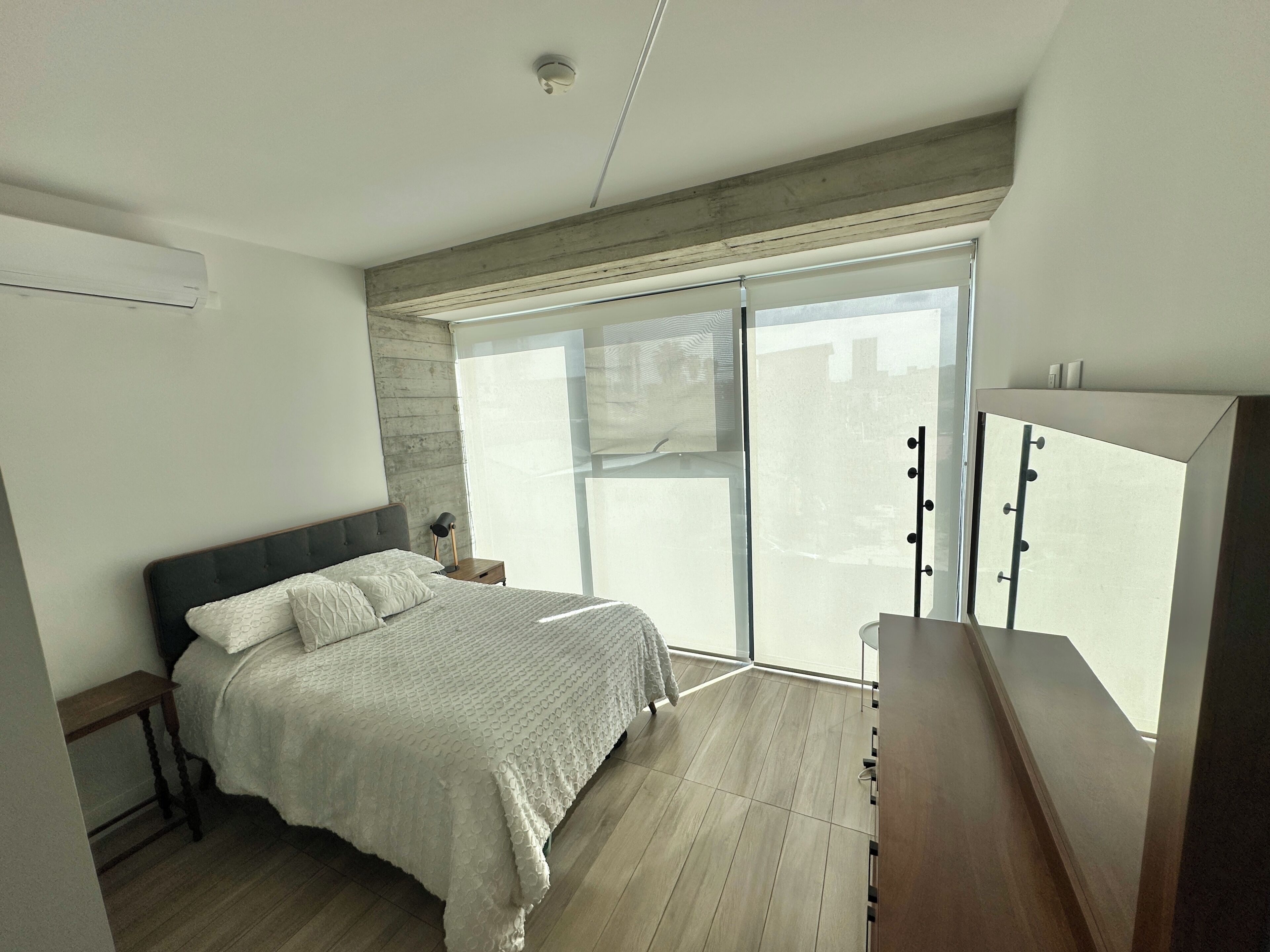 A bedroom with a bed, bedside table, lamp, and a large window.