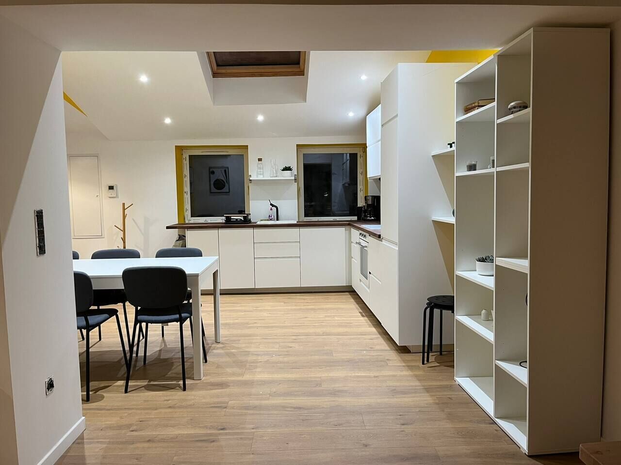 A modern kitchen with white cabinets, a dining table with chairs, and a built-in bookshelf.
