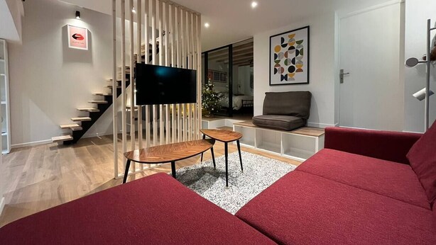 A modern living room with a staircase, a flat-screen TV, a red sofa, and a coffee table. - La Botte - 2-Bedroom Apartment, Downtown Épinal (Épinal)