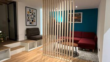 Een moderne woonkamer met een houten scheidingswand, een bruine bank, een rode bank en een salontafel.