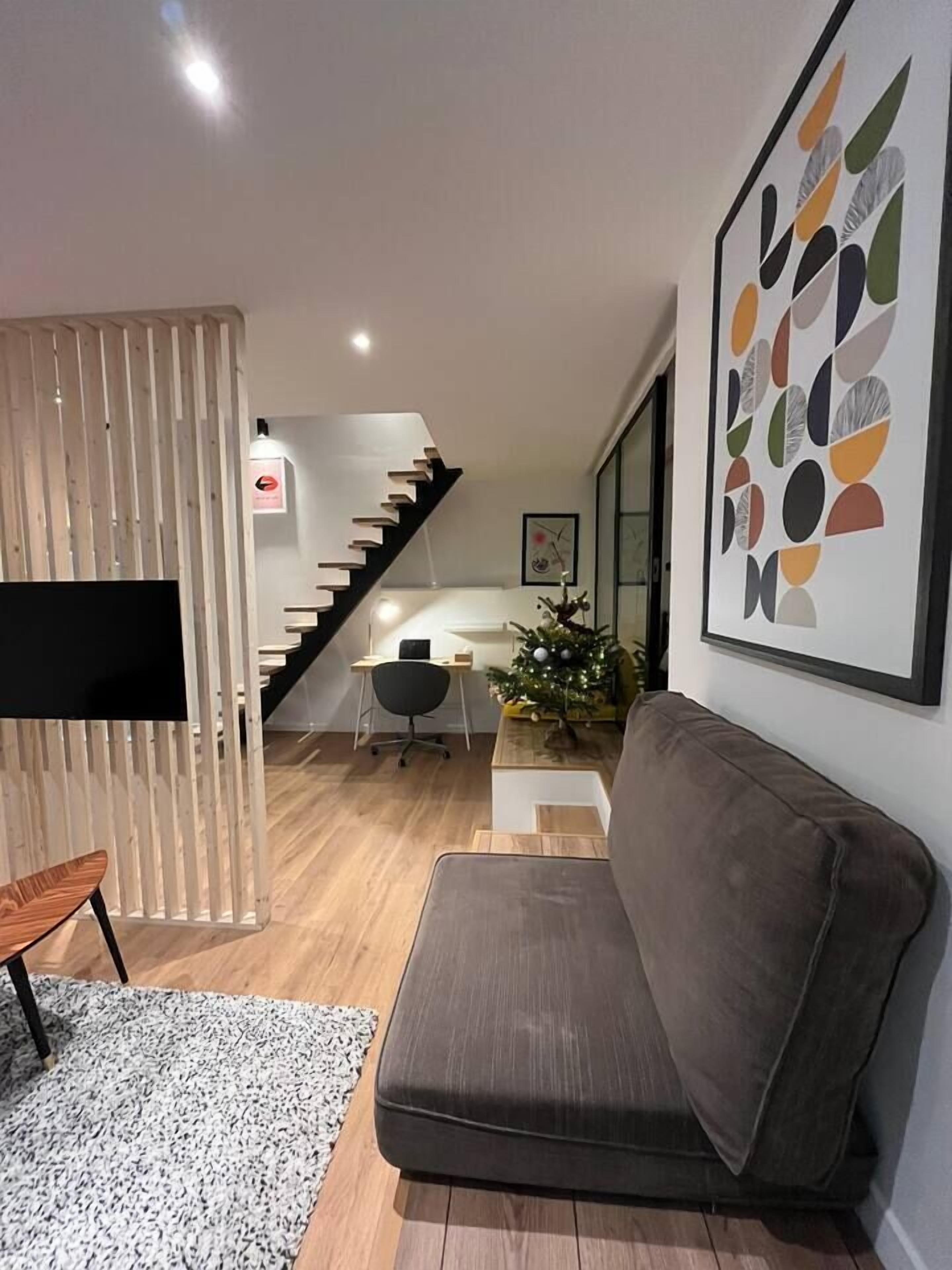 A modern living room with a sofa, a TV, a staircase, and a Christmas tree.