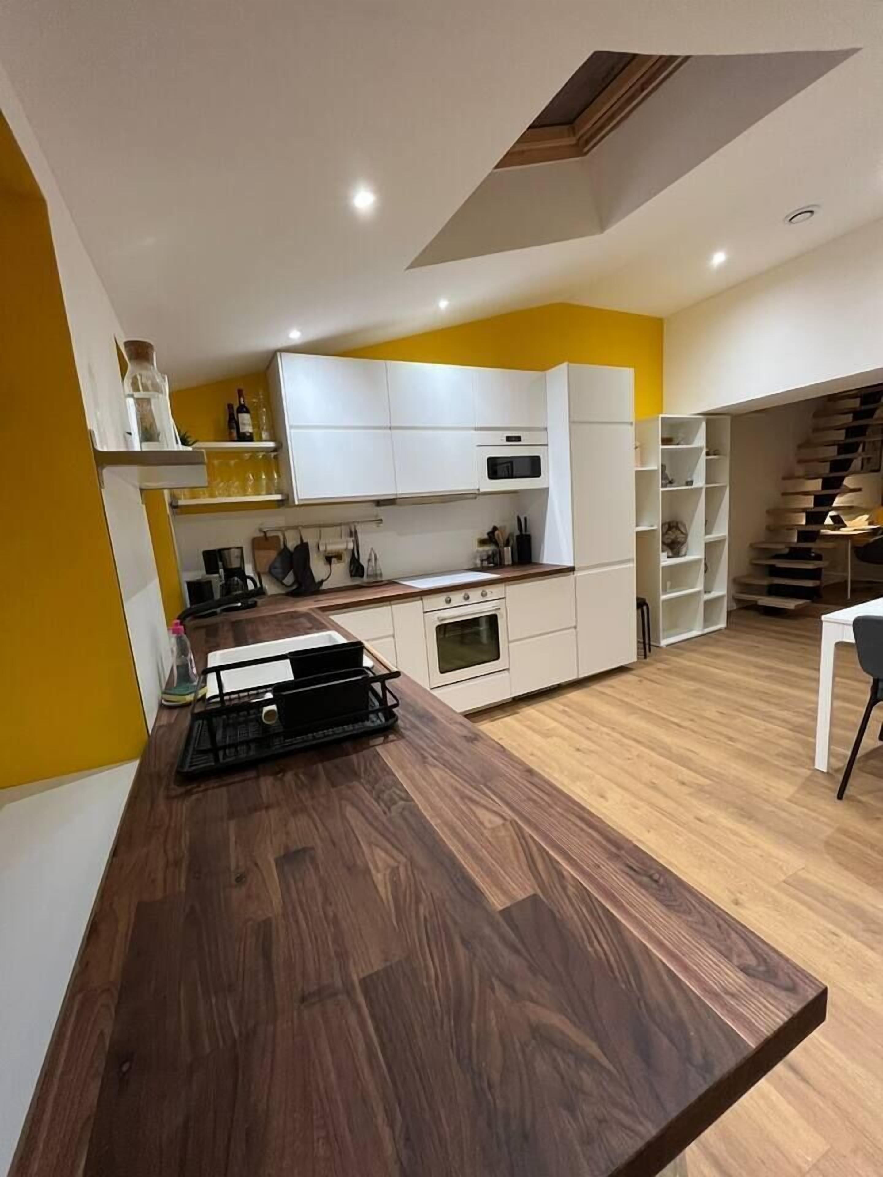 Una cocina moderna con armarios blancos, encimera de madera y horno empotrado.