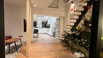 Een modern interieur met een houten vloer, een trap met kerstboom, en een keuken in de achtergrond.