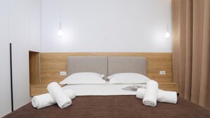 Ein ordentlich bezogenes Bett mit zwei Kissen und zwei aufgerollten Handtüchern, einem Holz-Kopfteil und zwei an der Wand befestigten Lampen.