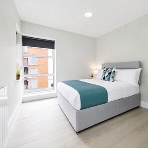 A modern bedroom with a bed, bedside table, lamp, and a view of a building through a window. - Modern Central Dublin Apartment  Near Bolton Square (Dublin 1)