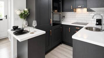Una cocina moderna con armarios oscuros, encimera blanca, electrodomésticos de acero inoxidable y una lámpara colgante.