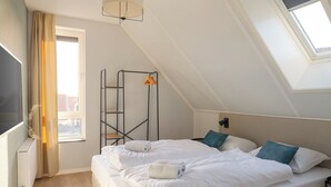 Quarto com cama, radiador, janela com cortinas e claraboia.