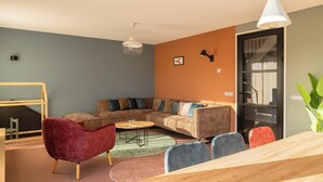 Uma sala de estar moderna com sofá em formato de L, uma poltrona vermelha, uma mesa de jantar de madeira e uma janela grande.