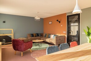 Ein modernes Wohnzimmer mit einer Eckcouch, einem roten Sessel, einem Holzessttisch und einem großen Fenster.