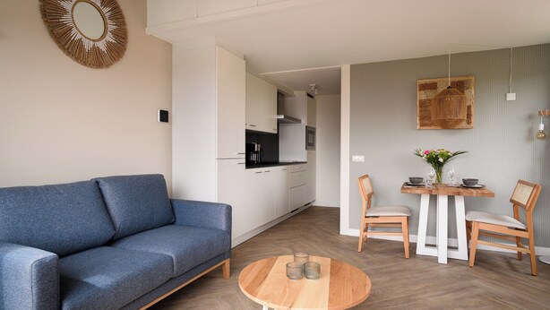 Ein modernes Wohnzimmer mit einer Couch, einem Esstisch mit Stühlen und einer Küche im Hintergrund.