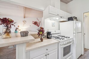 A kitchen with white cabinets, a gas stove, a refrigerator, and decorative items on the counter. - Lovely 1-bedroom condo in Carpinteria steps from the beach (Carpinteria)