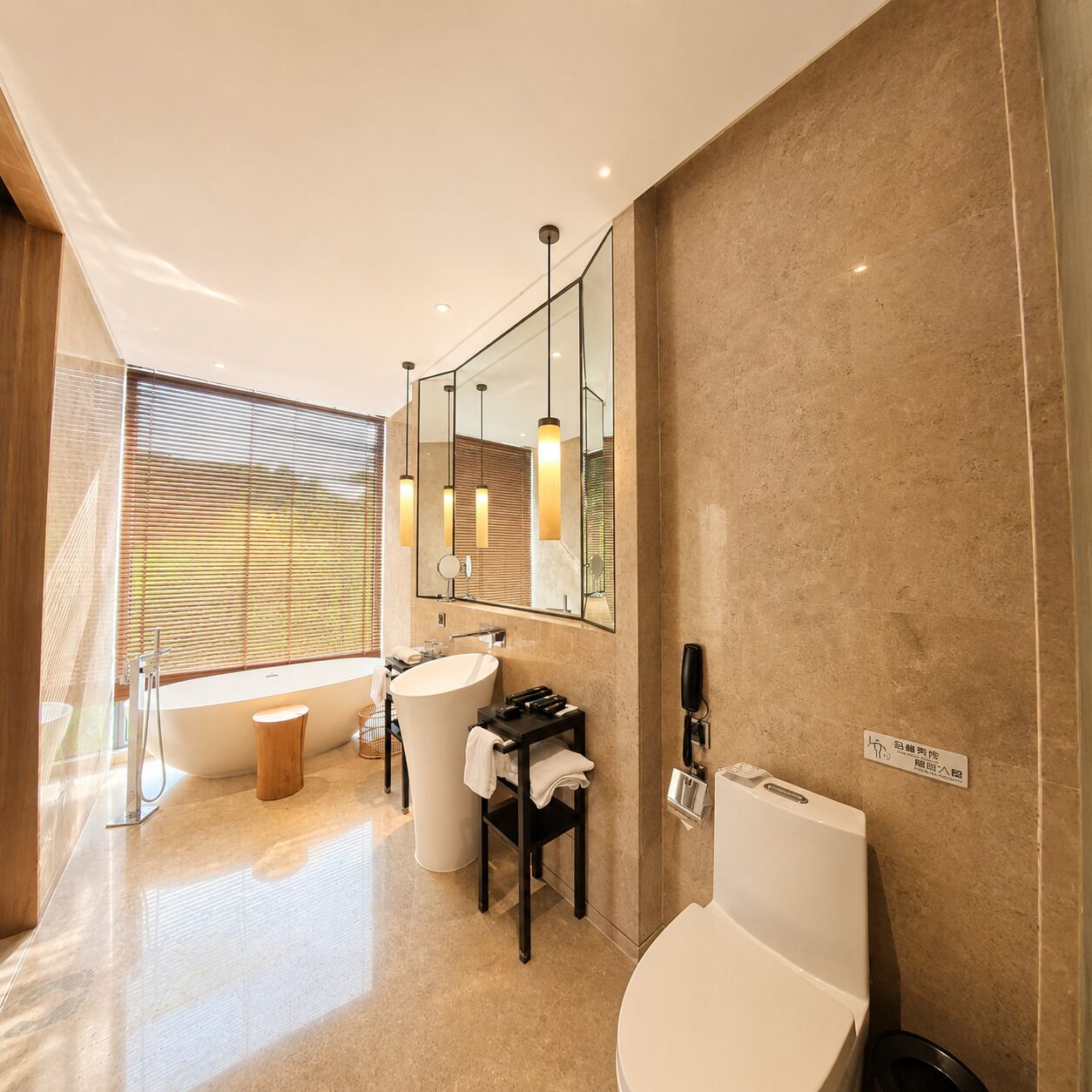 A modern bathroom with a large bathtub, a sink, and a toilet. There is a window with blinds, a mirror, and a towel rack.