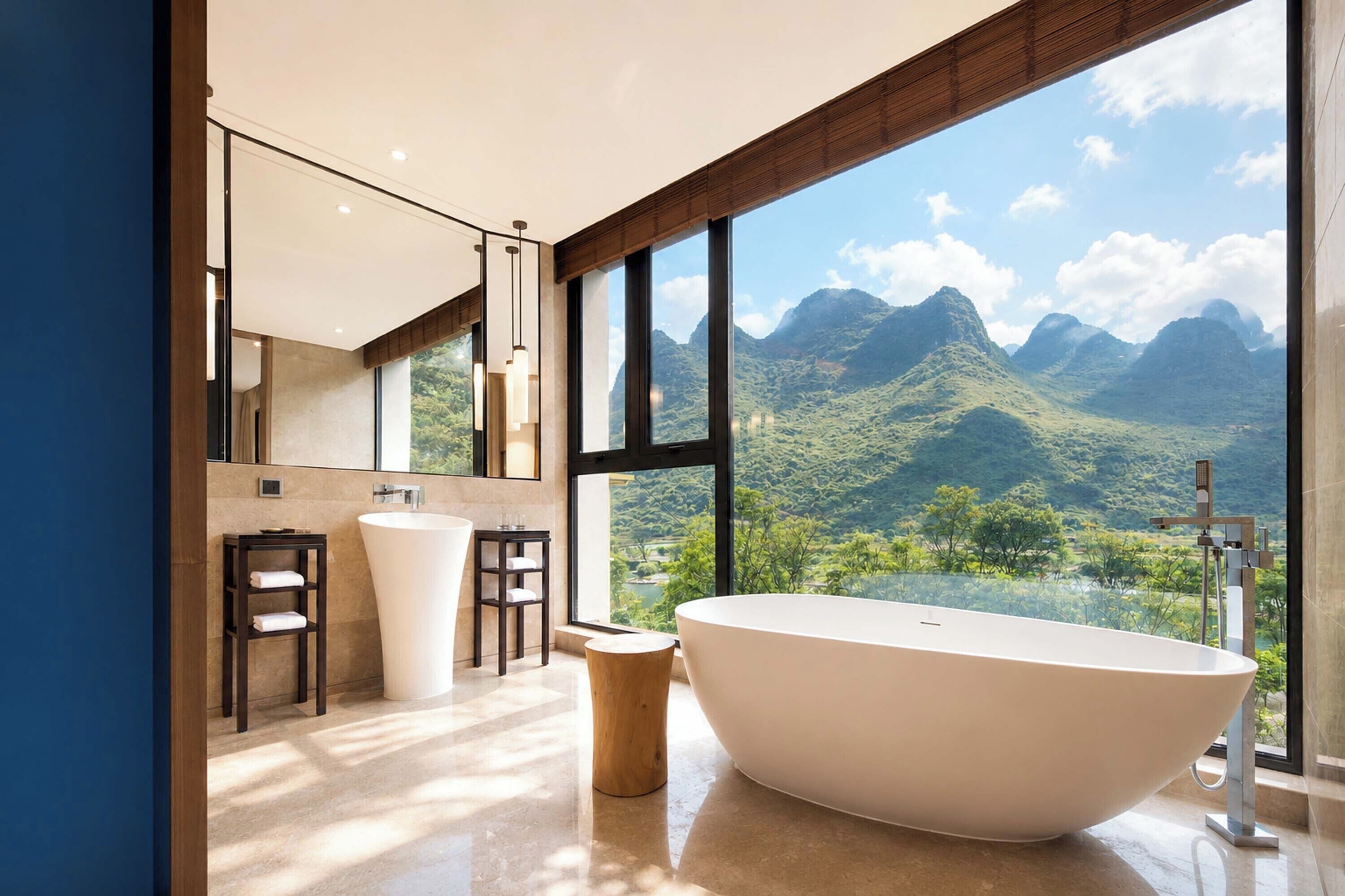 A modern bathroom with a freestanding bathtub, a large mirror, and a view of mountains.