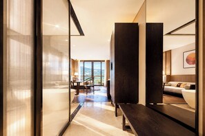Habitación de hotel moderna con un ventanal grande, un sofá, un área de comedor y un banco de madera.