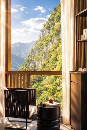 A balcony with a wooden chair, a small table with a teapot, and a view of a mountainous landscape. - The Blossom Dreamscape Boutique Hotel - Yulong River Branch - Free Buffet Breakfast & Laundry Facilities & Tailor Made Tours  (Guilin)