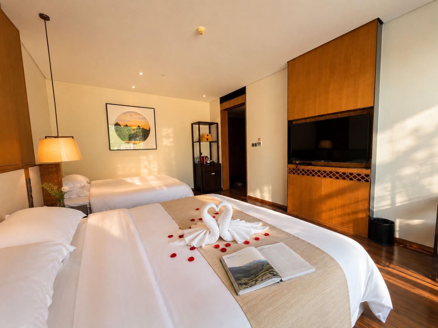A hotel room with two beds, a TV, a bookshelf, and a painting on the wall.