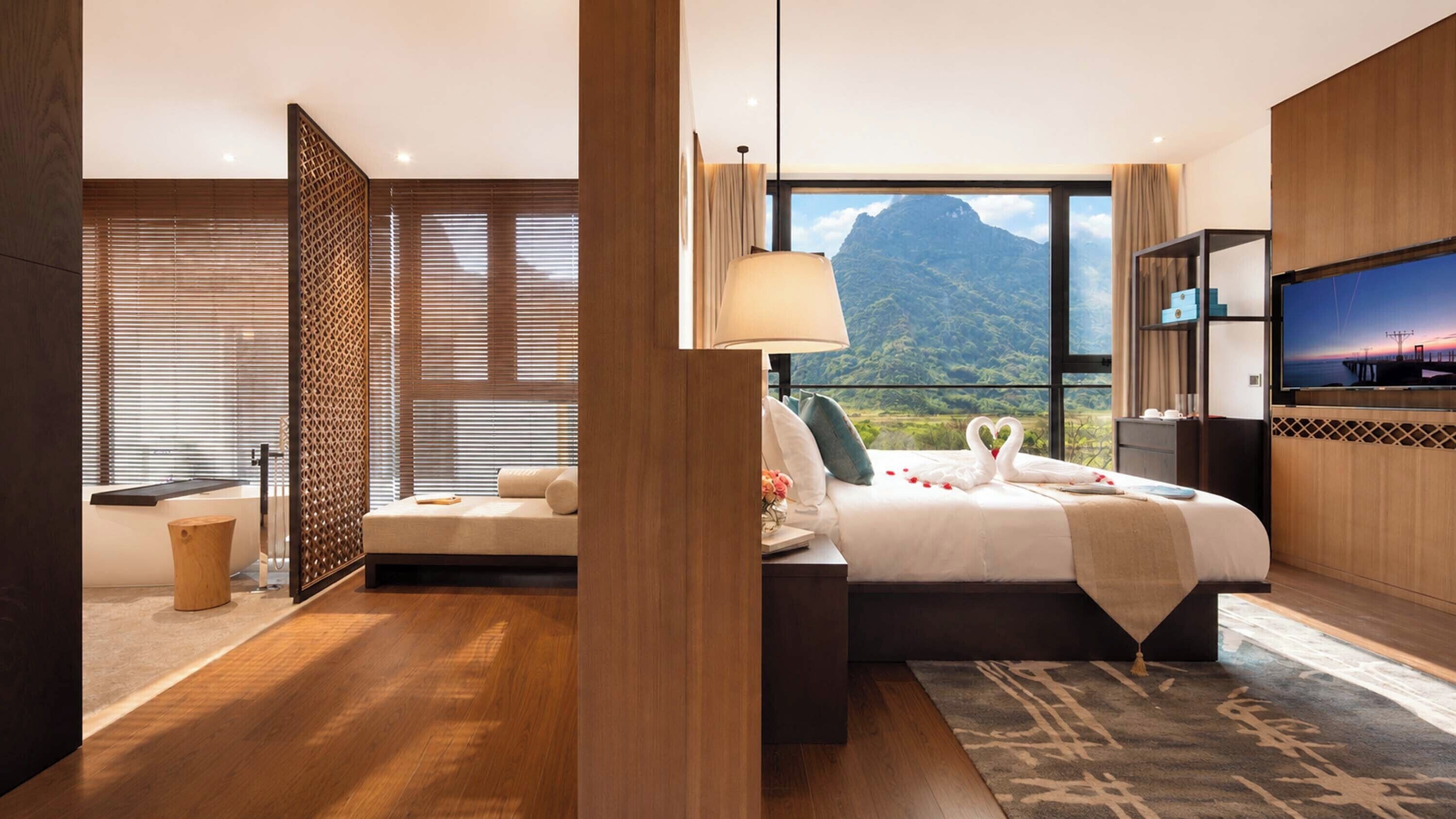 A modern hotel room with a large bed, a TV, and a view of mountains.