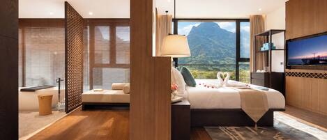 A modern hotel room with a large bed, a TV, and a view of mountains.
