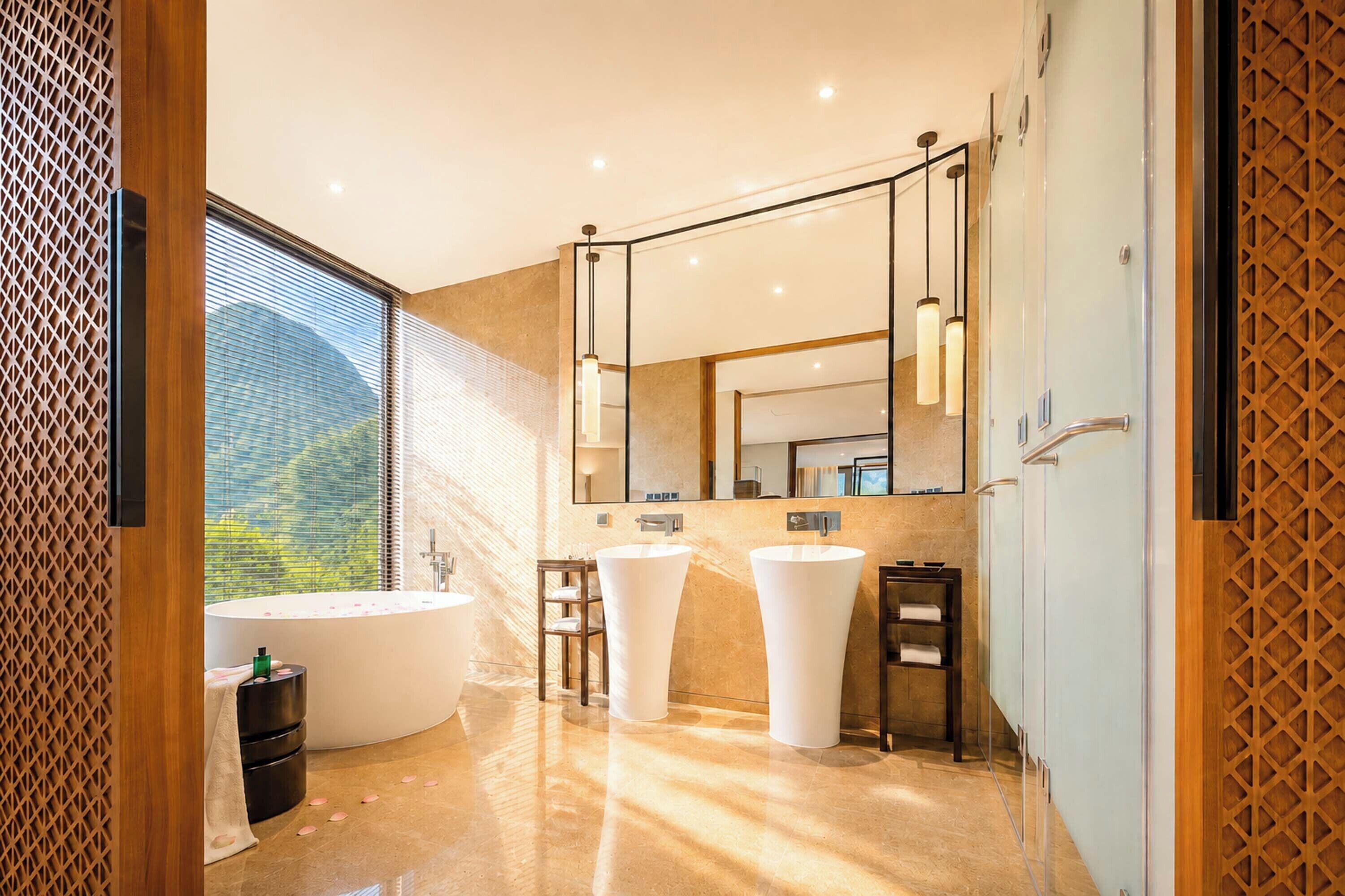 A modern bathroom with a large bathtub, two sinks, a mirror, and a view of a mountain.