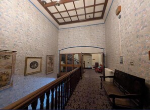 A hallway with patterned wallpaper, a wooden railing, a bench, and framed pictures on the walls. - Superior Double or Twin Room (Burton on Trent)