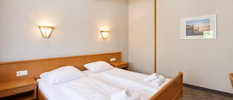 A hotel room with a double bed, two bedside tables, a wooden headboard, two wall-mounted lights, a framed picture on the wall, and a carpeted floor.