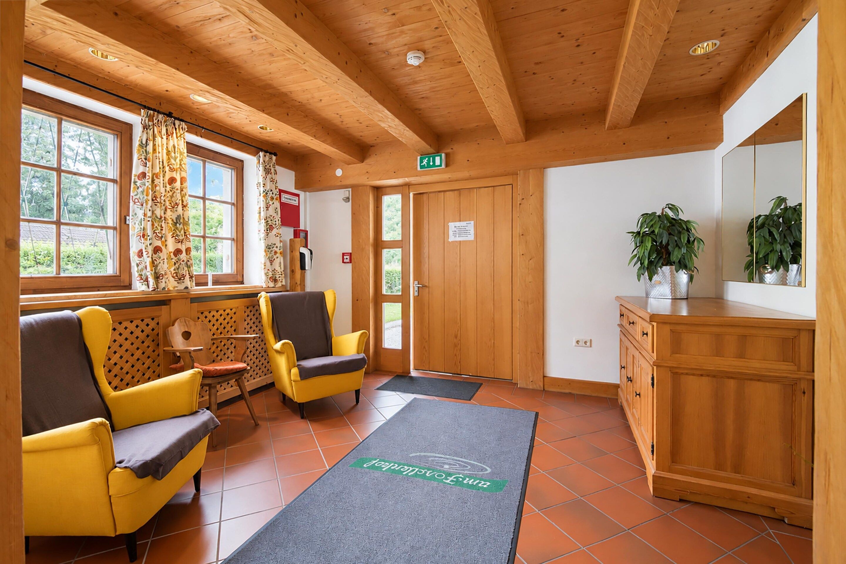 Una habitación con vigas de madera en el techo, dos sillas amarillas, un armario de madera y una puerta con señal de salida.