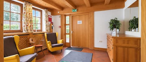 Une pièce avec des poutres en bois au plafond, deux chaises jaunes, un meuble en bois et une porte sur laquelle est apposée une signalétique indiquant la sortie.