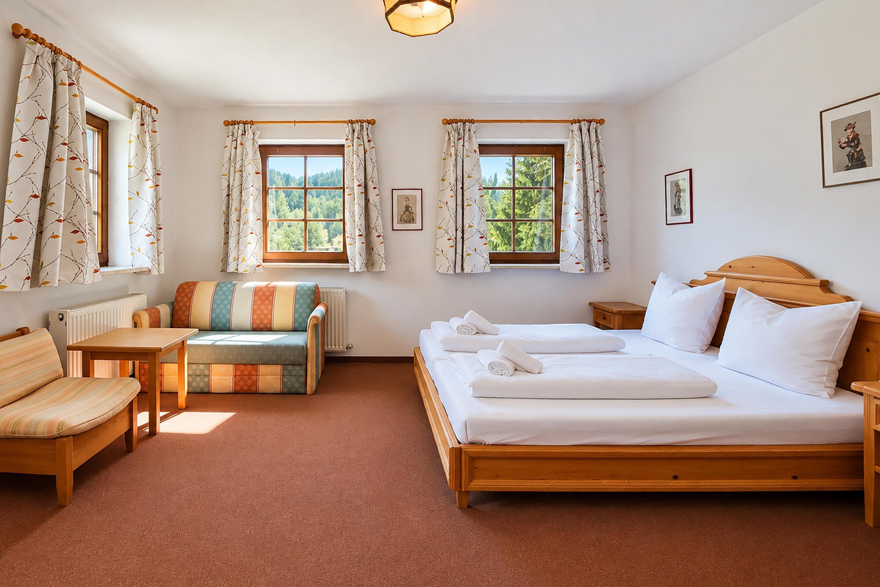 A room with a bed, two bedside tables, a sofa, a chair, and two windows with curtains.