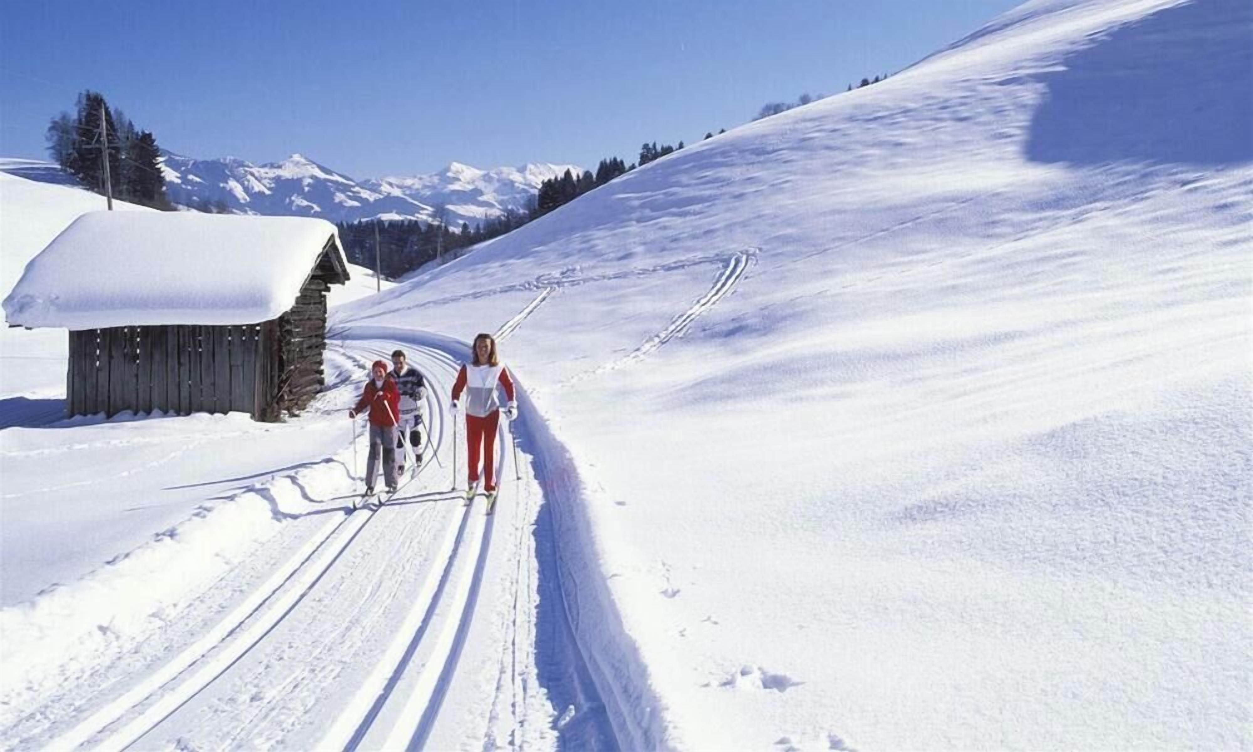 Una senda nevada para esquiar con una cabaña de madera y cielo despejado.