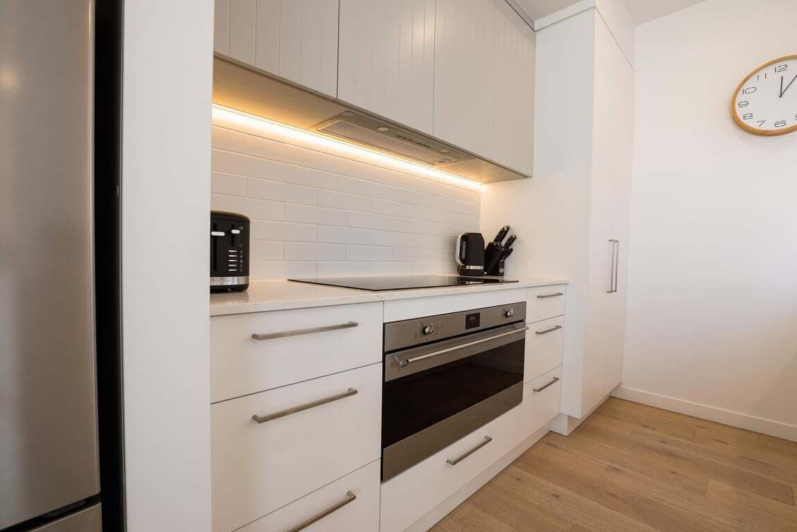 Una cocina moderna con armarios blancos, horno empotrado y cafetera sobre la encimera.