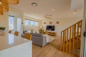 Een moderne woonkamer met een grijze bank, een televisie, een eethoek met een tafel en stoelen, en een trap.
