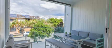 A balcony with a table and seating, a ceiling fan, and a view of a residential area with solar panels.