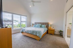 Ein Schlafzimmer mit großem Fenster, einem Bett, einem Nachttisch und einem Deckenventilator.