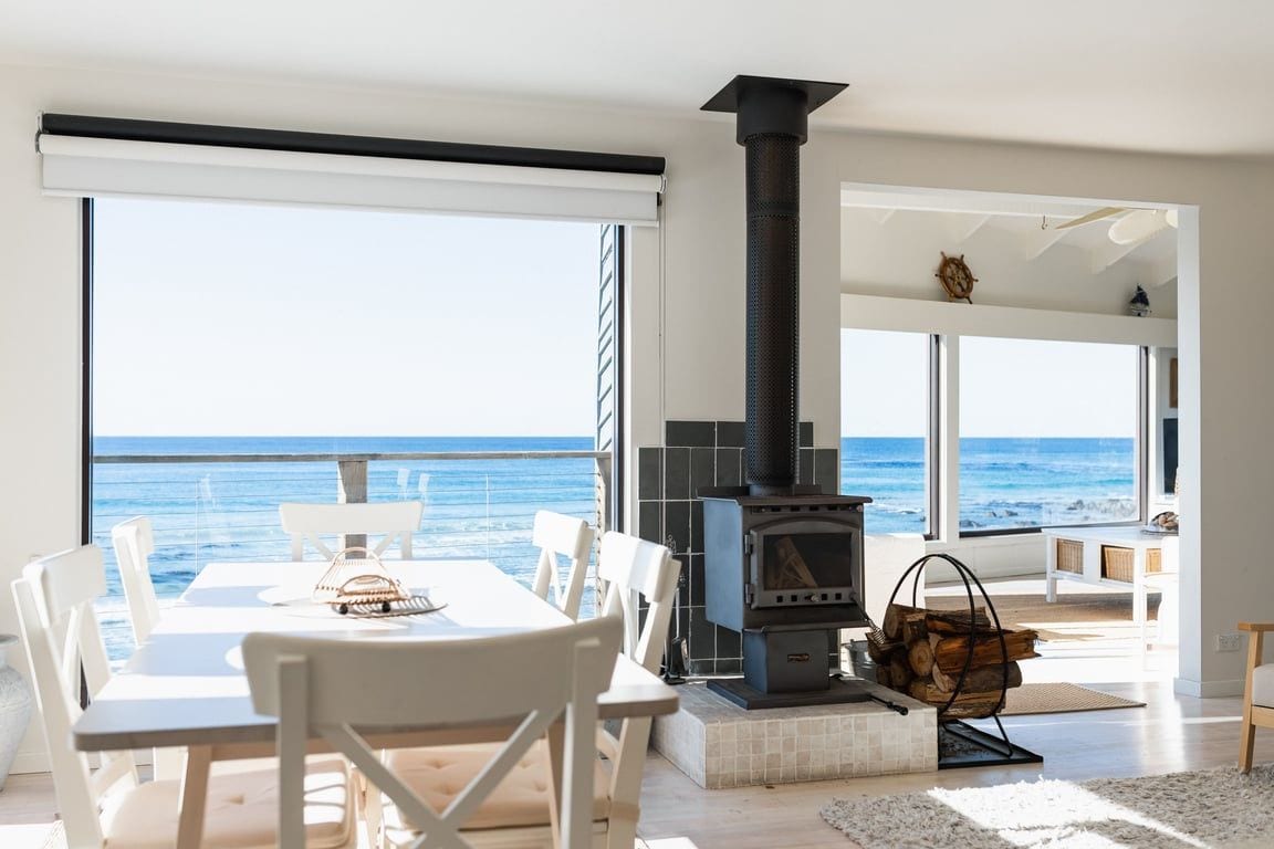 A spacious room with a large table and chairs, a fireplace, and a view of the ocean.